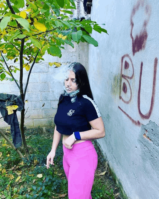 a woman smoking a cigarette in front of a wall that has the letter bu written on it