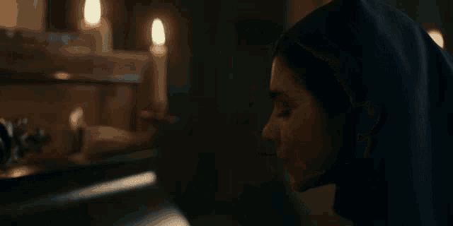 a woman in a nun 's robe is standing in a dark room with candles