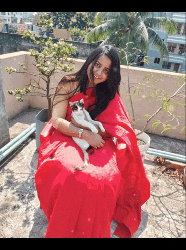 a woman in a red dress is holding a cat on her lap