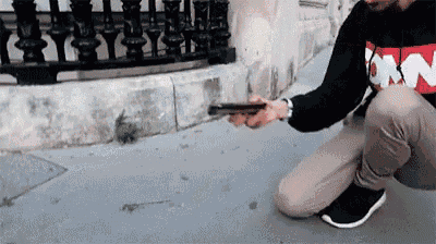 a man is squatting down on the sidewalk while holding a cell phone in his hand .