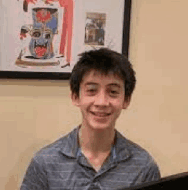 a young boy is smiling while sitting in front of a computer in front of a picture on the wall .