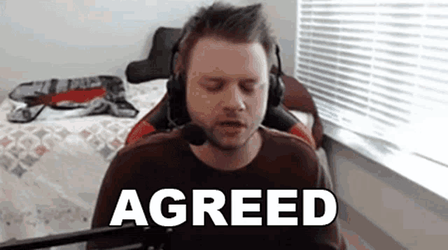a man wearing headphones and a microphone is sitting in front of a microphone with the word agreed on the screen .