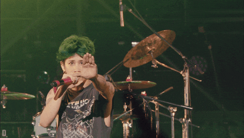 a man with green hair is singing into a microphone while wearing a shirt that says static shock