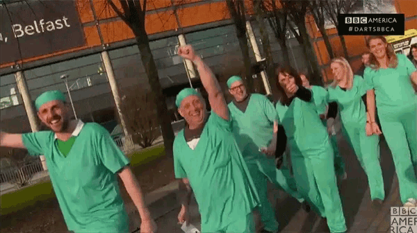 a group of people wearing green scrubs are dancing in front of a belfast sign