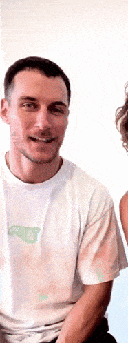 a man wearing a white t-shirt with a green sticker on it