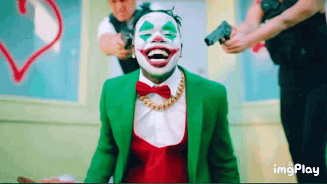 a man in a clown costume is laughing while a police officer holds a gun in the background