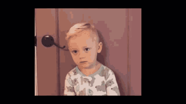 a little boy is standing in front of a door and looking at something .