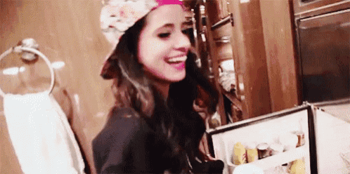 a woman wearing a hat is laughing while looking at a fridge .