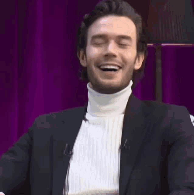 a man wearing a white turtleneck and a black jacket smiles