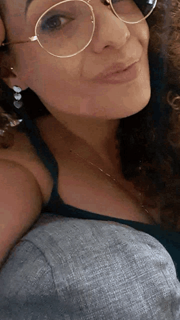 a woman with curly hair wearing glasses and earrings looks at the camera