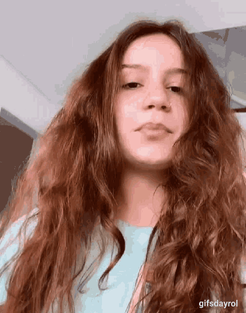 a girl with long red hair is wearing a blue shirt and making a funny face .