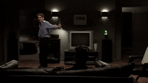 a man standing next to a man sitting on a couch in front of a television