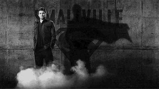 a black and white photo of a man standing in front of a wall with a shadow of superman on it .
