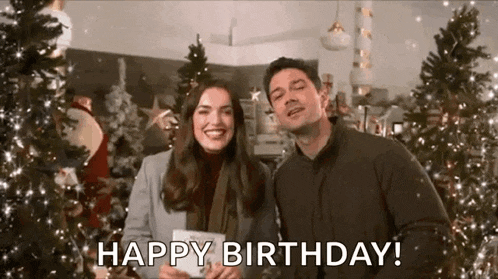 a man and a woman are standing next to each other in front of a christmas tree and smiling .