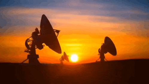 two satellite dishes are silhouetted against the sun at sunset