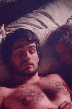a man without a shirt is laying on a bed with a woman .