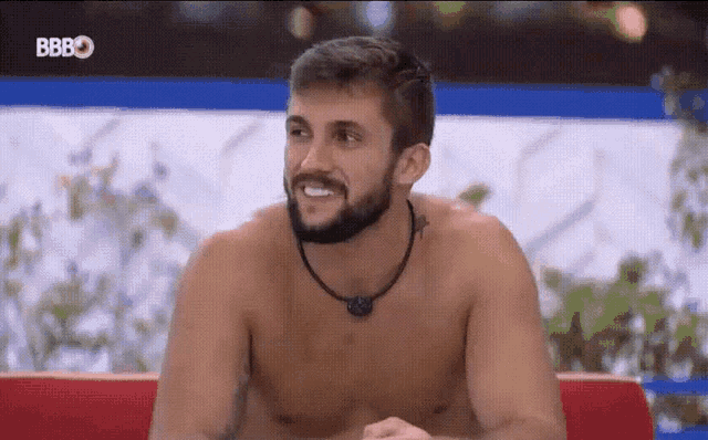 a shirtless man with a beard is sitting on a red couch in front of a sign that says bbbo