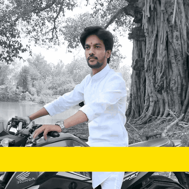 a man sitting on a honda motorcycle with a tree in the background