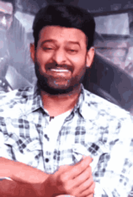 a man with a beard wearing a plaid shirt smiles with his eyes closed