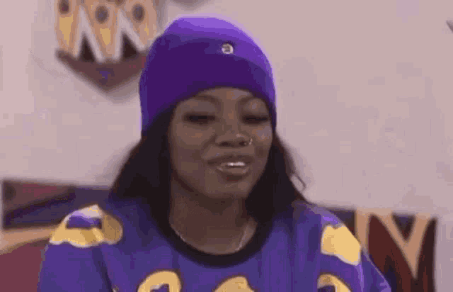 a woman wearing a purple hat and a blue shirt is smiling .