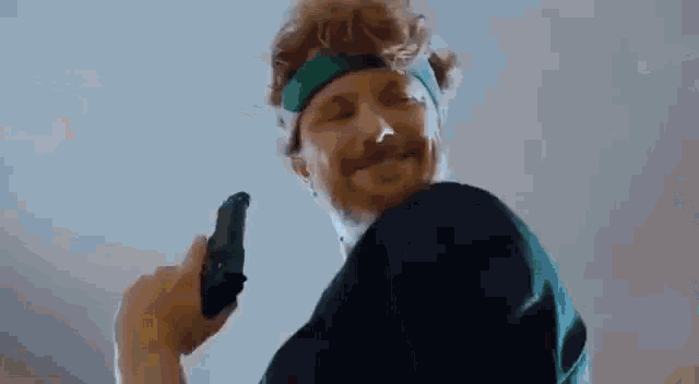 a man wearing a green headband is holding a gun in his hand .