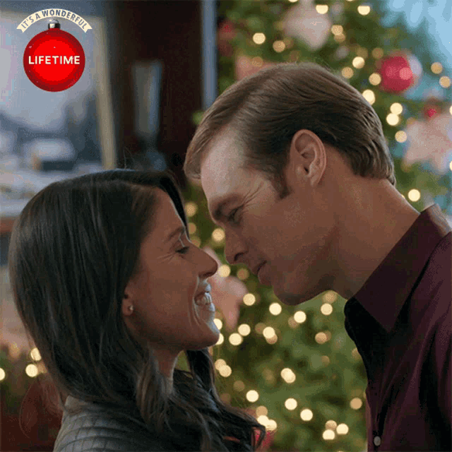 a man and a woman are kissing in front of a lifetime christmas ornament