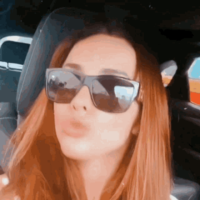 a woman wearing sunglasses is sitting in a car and blowing a kiss