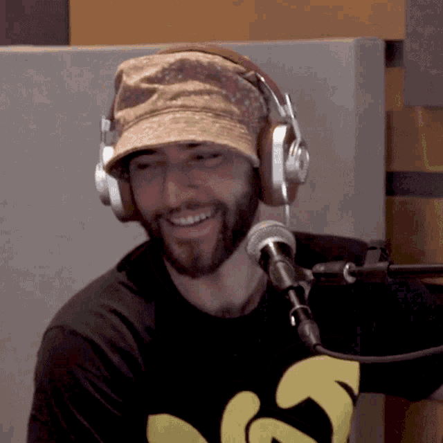 a man wearing a hat and headphones stands in front of a microphone