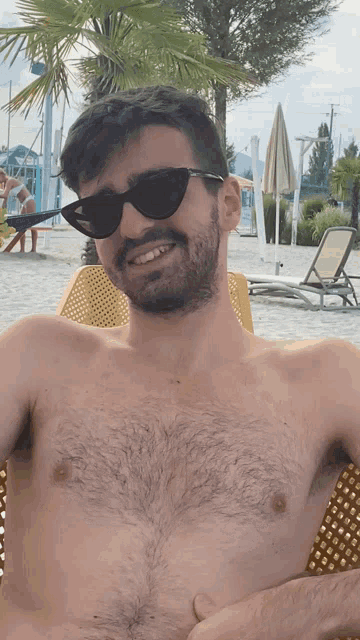 a shirtless man wearing sunglasses sits on the beach