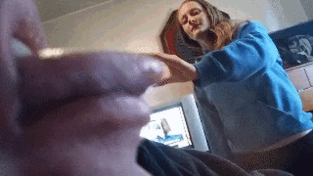 a woman in a blue sweater holds a man 's hand in a living room