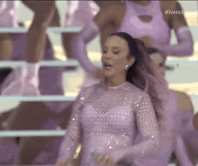 a woman in a purple dress is dancing on a stage with other women .