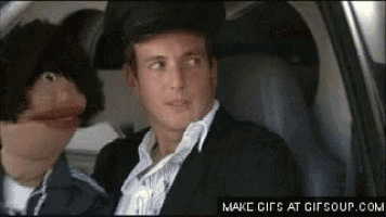 a man in a suit is sitting in a car with a puppet behind him .