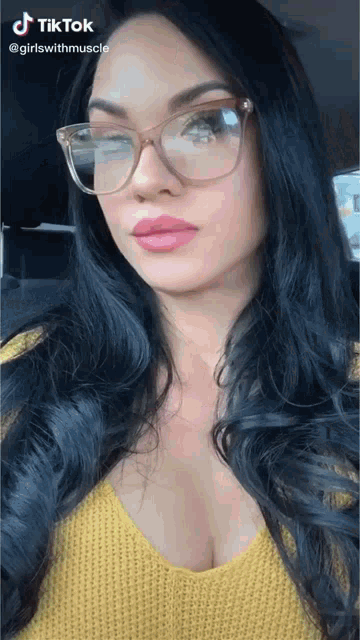 a woman wearing glasses and a yellow sweater is sitting in a car .