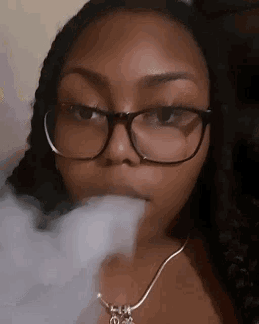 a woman wearing glasses is blowing smoke out of her mouth .