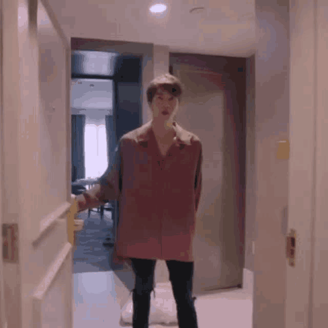 a young man in a pink shirt is standing in a hallway .