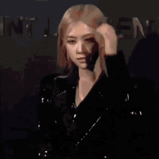 a woman with blonde hair is wearing a black jacket and adjusting her hair .