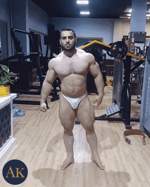 a man in a white bikini is standing in a gym with the letters ak behind him