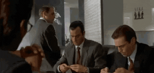 a group of men in suits and ties are sitting around a table in an office