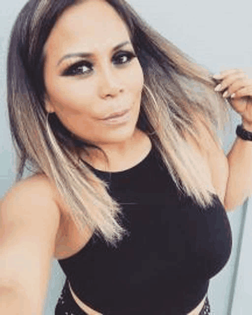 a woman in a black tank top is taking a selfie with her hair in her hand .