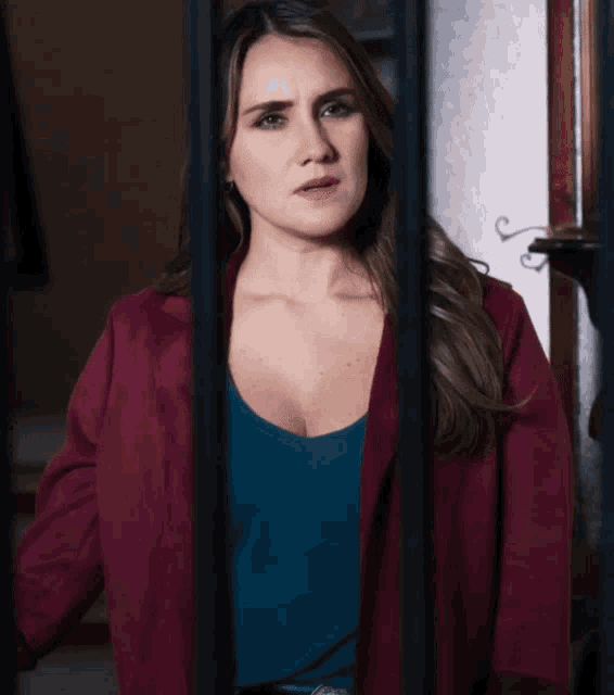 a woman in a burgundy jacket and a blue shirt is behind bars