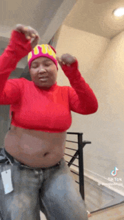 a woman wearing a red crop top and a pink hat is dancing .