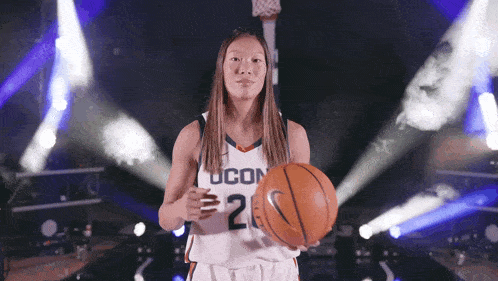 a woman in a ucon jersey holds a basketball in her hands