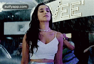 a woman in a white crop top is standing in the rain in front of a store .
