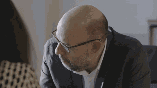 a bald man with glasses and a beard is looking down