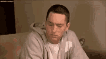 a man in a gray hoodie is sitting on a couch with his eyes closed