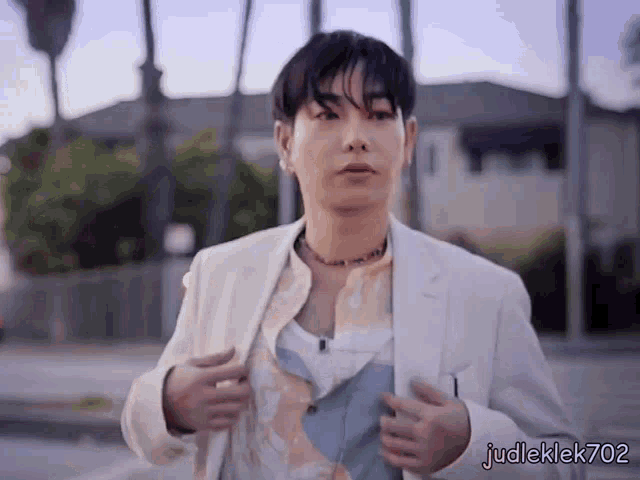 a man wearing a white jacket and a necklace with judleklek702 on the bottom