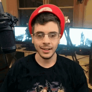 a man wearing glasses and a red hat is standing in front of a microphone