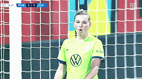 a woman in a vw shirt stands in front of a soccer goal