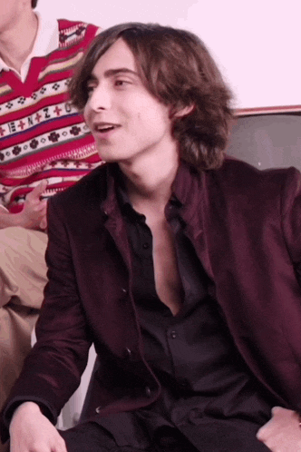 a young man with long hair is wearing a burgundy jacket
