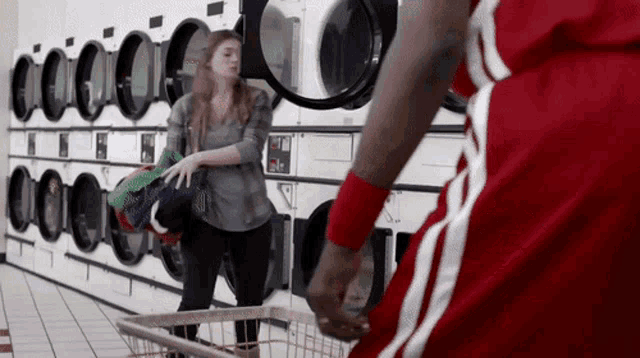 a man in a red shirt is standing in a laundromat next to a woman in a basket